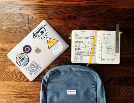 Computador, mochila e caderno dispostos na mesa